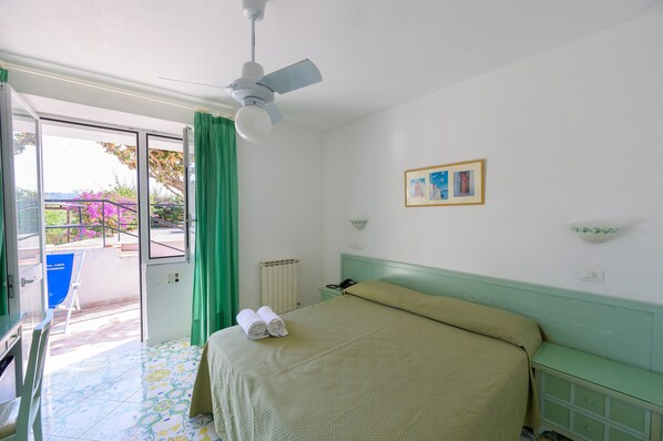 A hotel room with a bed, a ceiling fan, a window with curtains, a small table, and a chair. - Hotel Parco Cartaromana (Ischia)