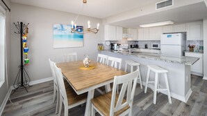 A modern kitchen with white cabinetry, a central island, and a dining area with a wooden table and white chairs.