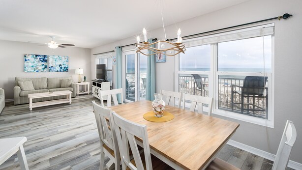 A modern living room with a wooden dining table, white chairs, a sofa, and a TV.
