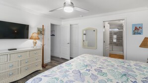 A bedroom with a bed, a television, a dresser, a mirror, and a shower. - PETE'S PARADISE IS MODERN, SPACIOUS FLOOR PLAN! GREAT FENCED IN BACKYARD WITH FIREPIT, PET FRIENDLY! (Port Saint Joe)