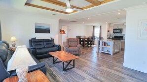 A living room with a sofa, armchair, and coffee table, a dining area with chairs, and a kitchen with appliances. - PETE'S PARADISE IS MODERN, SPACIOUS FLOOR PLAN! GREAT FENCED IN BACKYARD WITH FIREPIT, PET FRIENDLY! (Port Saint Joe)