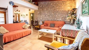 Un salon chaleureux avec un mur en pierre, un canapé, une table basse et une nappe à motifs.