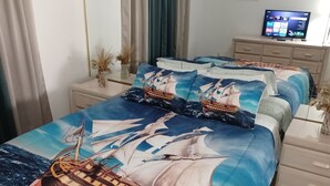 Ein Schlafzimmer mit einem Bett, das mit einem Bezug im Marine-Stil ausgestattet ist, einem an der Wand befestigten Fernseher und einem Deckenventilator.