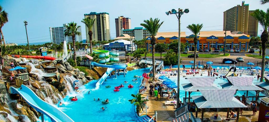 Een waterpark met meerdere glijbanen en zwembaden, omgeven door palmbomen en gebouwen.