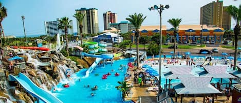 Een waterpark met meerdere glijbanen en zwembaden, omgeven door palmbomen en gebouwen.