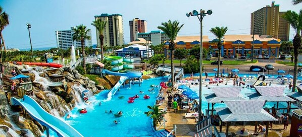Un parque acuático con varias toboganes y piscinas, rodeado de palmeras y edificios.