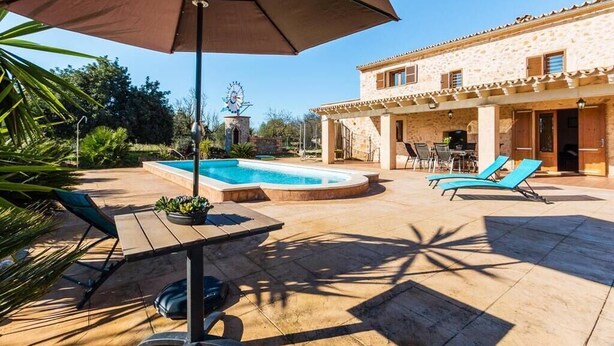 A pool area with a stone building, lounge chairs, and a windmill in the background. - Villa Capo, Charming villa located in a peaceful rural area (Sa Pobla)