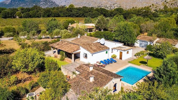 A villa with a swimming pool, surrounded by lush greenery and mountains in the background.