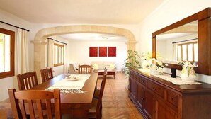 A dining area with a wooden table and chairs, a sofa, and a cabinet with decorative items.