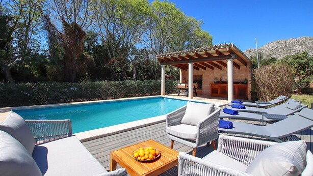 Un espace aménagé au bord de la piscine, avec des chaises longues, une table en bois sur laquelle sont disposés des fruits et une structure en forme de pergola.