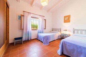 Un dormitorio con dos camas individuales, una mesita pequeña, un banco y una ventana con cortinas.
