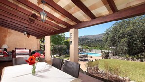 A covered patio with a table set for dining, a pool in the background, and a view of the surrounding landscape. - Villa Porqueres, Charming house with pool near Pollensa (Pollença)