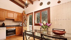 A kitchen with wooden cabinets, a glass dining table, and a stone wall. - Villa Porqueres, Charming house with pool near Pollensa (Pollença)