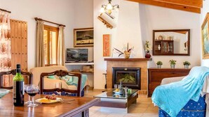 A cozy living room with a fireplace, wooden furniture, and a dining area with a table set for two. - Villa Geroni, Charming 3 bedroomn villa with pool (Pollença)
