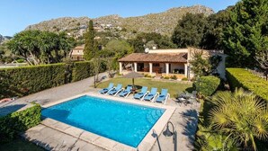 A pool area with lounge chairs, a house with a tiled roof, and a mountainous backdrop. - Villa Geroni, Charming 3 bedroomn villa with pool (Pollença)