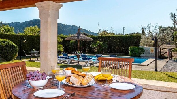 An outdoor dining area with a table set for breakfast, overlooking a swimming pool and mountains. - Villa Geroni, Charming 3 bedroomn villa with pool (Pollença)