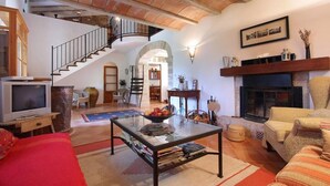 A spacious living room with a fireplace, a staircase, and a television. - Ca'n Pascol, Villa over 250 years old in a breathtaking setting (Pollença)