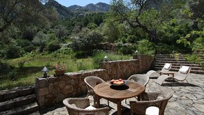 A stone patio with wicker furniture and a table set with fruit, overlooking a mountainous landscape. - Ca'n Pascol, Villa over 250 years old in a breathtaking setting (Pollença)