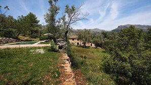A rustic stone pathway leading to a traditional stone building surrounded by lush greenery and a clear blue sky. - Ca'n Pascol, Villa over 250 years old in a breathtaking setting (Pollença)