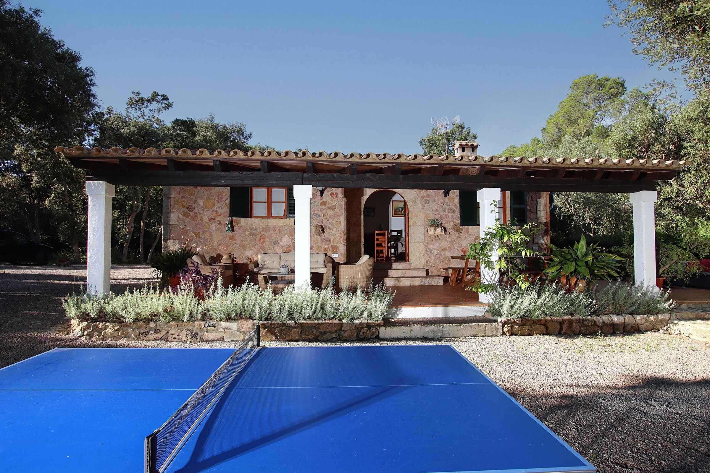 A house with a stone exterior, a covered patio, and a blue outdoor table tennis table.
