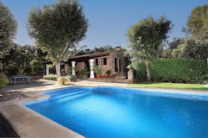 A swimming pool with a stone house in the background, surrounded by greenery.