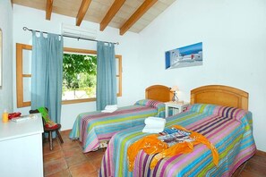 A room with two beds, a desk, and a chair. There is a window with curtains, a picture on the wall, and a view of greenery outside. - Villa Burgues, Idyllic location affording beautiful views. Alcudia (Alcúdia)