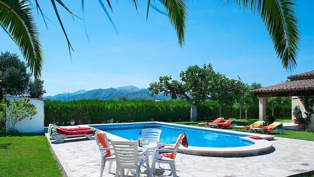 A swimming pool with lounge chairs and a table, surrounded by greenery and a view of mountains. - Villa Burgues, Idyllic location affording beautiful views. Alcudia (Alcúdia)