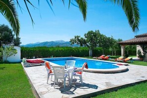 A swimming pool with lounge chairs and a table, surrounded by greenery and a view of mountains. - Villa Burgues, Idyllic location affording beautiful views. Alcudia (Alcúdia)