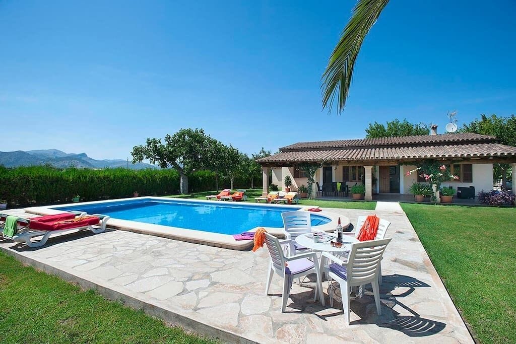 A pool area with lounge chairs, a table, and a building with a tiled roof.