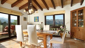 A dining area with a wooden table and chairs, a chandelier, and a view of mountains through large windows. - Villa LLop, Magnificent modern villa with sauna (Pollença)