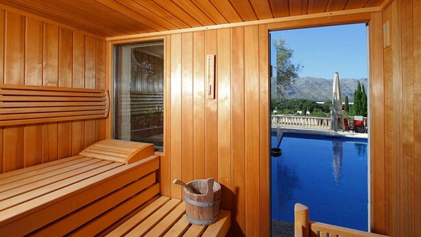 A wooden sauna with a bench and a bucket, overlooking a swimming pool with mountains in the background. - Villa LLop, Magnificent modern villa with sauna (Pollença)