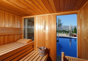 A wooden sauna with a bench and a bucket, overlooking a swimming pool with mountains in the background. - Villa LLop, Magnificent modern villa with sauna (Pollença)