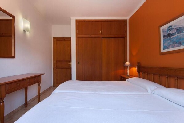 Une chambre à coucher avec un lit en bois, une table de chevet avec une lampe, un bureau en bois et une armoire.