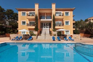Un hôtel à plusieurs étages doté d’une piscine, de chaises longues et d’un escalier menant à l’entrée.