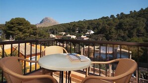 A balcony with wicker chairs and a table, overlooking a mountainous landscape with buildings in the background. - Pinos Altos 14 (T3) - Ciruelo, Cala Sant Vicenç (Cala Sant Vicenç)