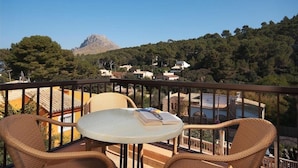 Un balcon avec des fauteuils et une table en osier, d’où l’on peut admirer un paysage montagneux avec des bâtiments en arrière-plan.