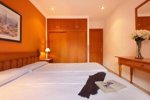 Une chambre d’hôtel avec deux lits, une armoire en bois, un bureau agrémenté d’un vase de fleurs et un tableau au mur.