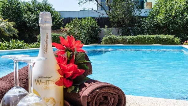 En hvidvinflaske, et glas og et sammenrullet håndklæde ved en pool.