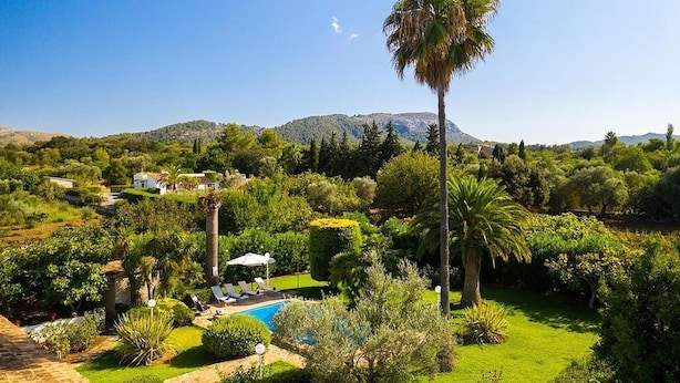 Un jardin luxuriant avec une piscine, des palmiers et une vue sur des collines lointaines.