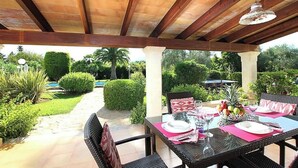Un espace patio extérieur avec une table dressée pour les repas, entouré de verdure et offrant une vue dégagée sur une piscine.