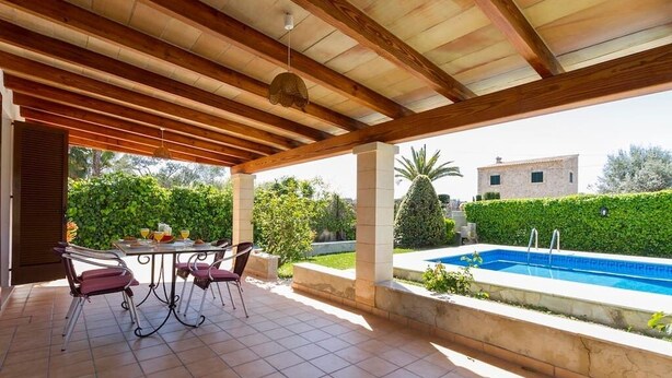 Une terrasse extérieure avec une piscine, un espace salon abrité et une vue sur la végétation et les bâtiments environnants.