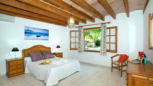Ein Schlafzimmer mit einem hölzernen Bett, einem Nachttisch, einem Schreibtisch, einem Stuhl, einem Fenster mit Vorhängen und einem Bild an der Wand.