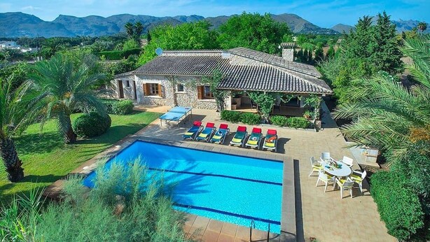 Ein Poolbereich mit einem Steinhaus, einem Schwimmbecken und einer Terrasse mit Stühlen und Tischen.