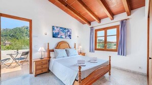 Un dormitorio con una cama de madera, una mesita de noche, una lámpara, una ventana con cortinas y vistas al exterior.