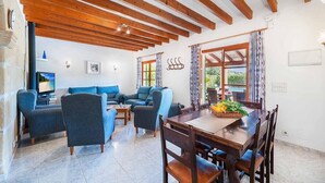 Una sala de estar con techo de madera, sofás azules, una mesa de comedor con sillas y una ventana con cortinas.