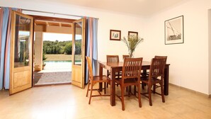 A dining area with a wooden table and chairs, a view of a swimming pool, and framed pictures on the wall. - Villa  Can Mares, Elegant and modern house designed with comfort and style (Pollença)