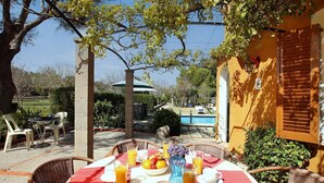 Preparación para el desayuno con una mesa, sillas y vistas a una piscina y jardín.