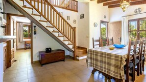 Amplia habitación con escalera de madera, una mesa de comedor con sillas y vistas al exterior.