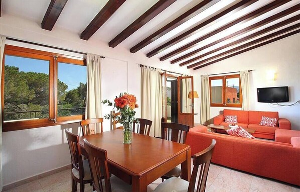 A room with a dining table, chairs, a sofa, and a TV.