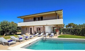 A two-story building with a swimming pool, sun loungers, and a covered patio area.